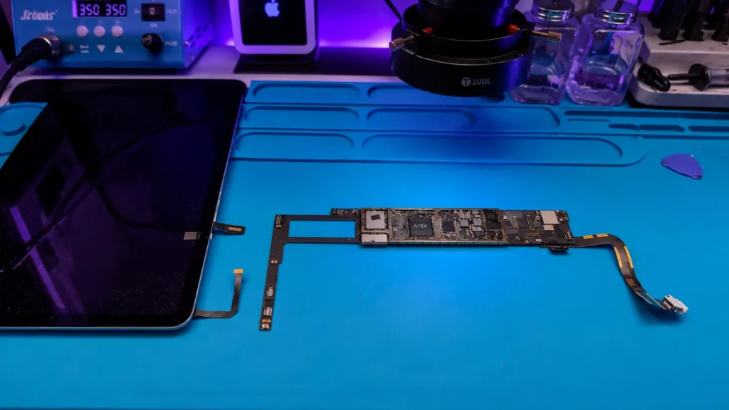 Disassembled iPad with the logic board exposed on a blue repair mat.